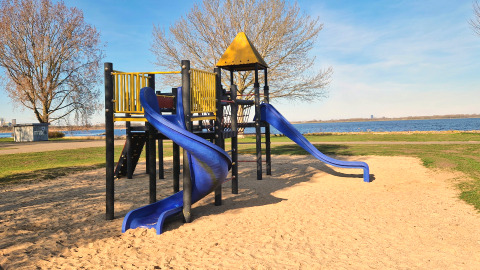 Spielplatz mit blauen Rutschen und gelbem Dach am Wasser, aufgenommen bei einer Glamping-Unterkunft.
