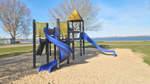 Spielplatz mit blauen Rutschen und gelbem Dach am Wasser, aufgenommen bei einer Glamping-Unterkunft.