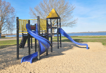 Parco giochi con scivoli blu vicino all’acqua, foto scattata presso una sistemazione glamping.