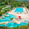 View of swimming pool, sun loungers and lush greenery at Camping Rosselba Le Palme holiday park in Tuscany, Italy.
