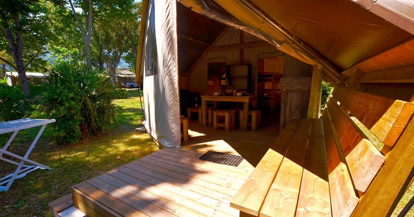Safaritent Tent Lodge Liberta bij Camping Merendella, Frankrijk, met houten terras en zitbank buiten.
