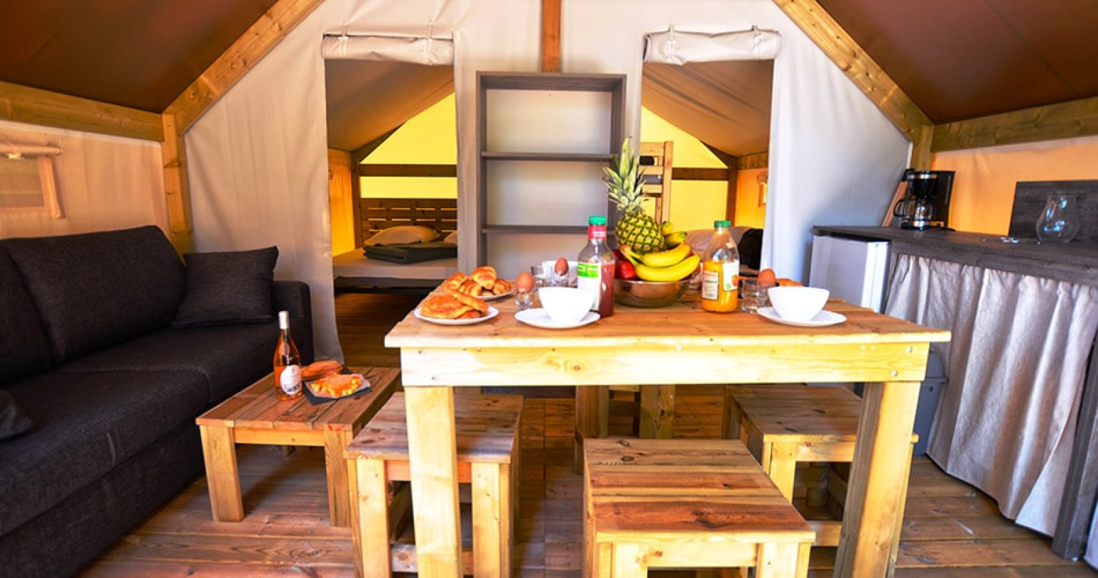 Binnenaanzicht van safaritent Liberta bij Camping Merendella in Frankrijk met eettafel en bank.
