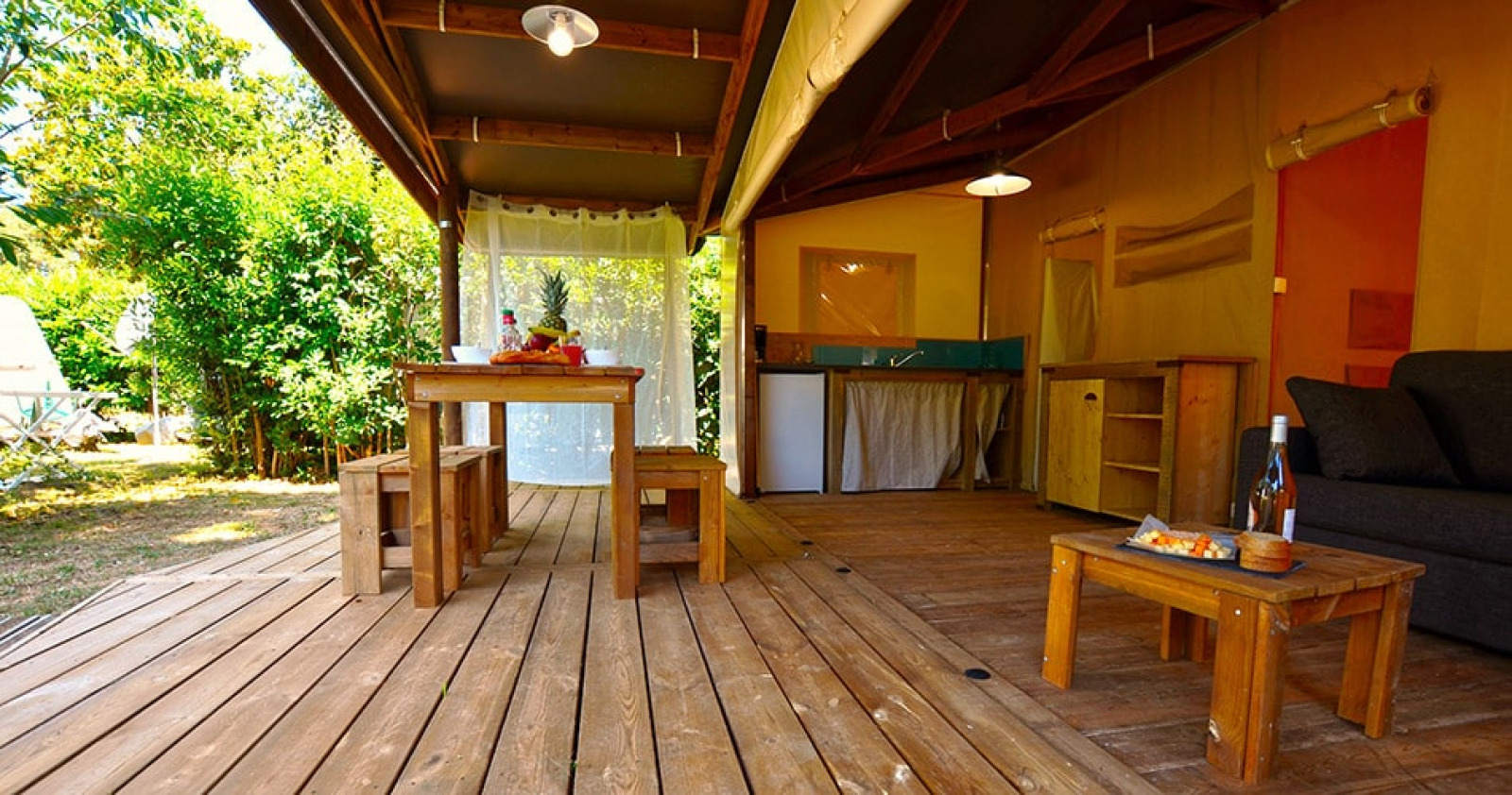 Houten terras en gezellige leefruimte in de Lodge Riada safaritent op Camping Merendella in Frankrijk.