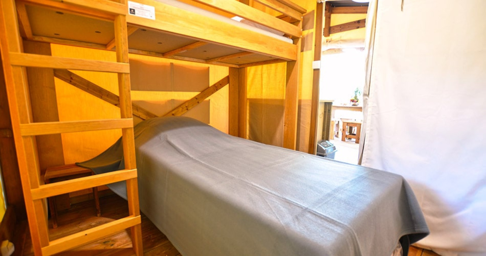 Binnenaanzicht van een safaritentlodge met stapelbed en eenpersoonsbed bij Camping Merendella in Frankrijk.