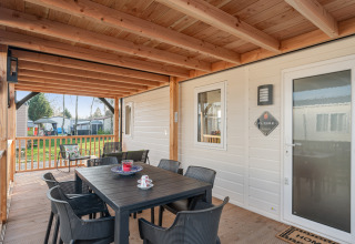 Veranda coperta del Vakantiehuis Admiral a Camping Papillon in Belgio, con tavolo da pranzo e sedie all’aperto.