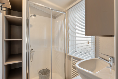 Bagno moderno e compatto con doccia in vetro, lavandino e finestra con persiane in un lodge in Belgio.