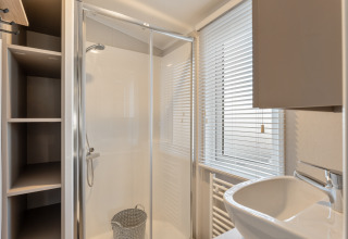 Bagno moderno e compatto con doccia in vetro, lavandino e finestra con persiane in un lodge in Belgio.