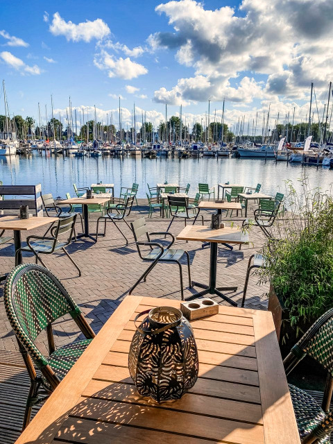 Außenterrasse mit Sitzplätzen und Blick auf einen Jachthafen bei Marina Parcs Naarden in den Niederlanden.