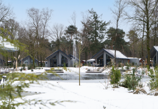 Snow-covered lodges by a lake at Ecovilla Waterzicht Comfort, Holiday park Latour, Netherlands.