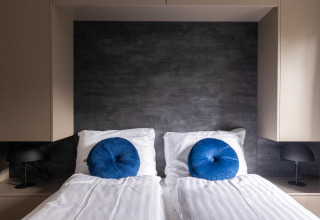 Dormitorio moderno en Ecovilla Waterzicht Comfort en los Países Bajos con dos camas y cojines azules redondos.