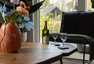 Botella de vino, dos copas y flores sobre una mesa en Ecovilla Waterzicht Comfort, Holiday park Latour, Países Bajos.