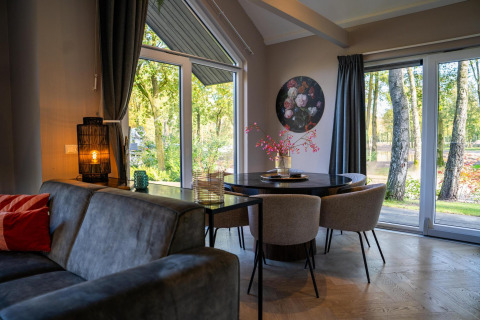 Modern lodge living and dining area with forest views, large windows, and cozy decor at Ecovilla Waterzicht Comfort.