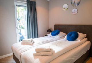 Camera moderna con letti singoli, cuscini blu e piatti decorativi all’Ecovilla Waterzicht Comfort nei Paesi Bassi.