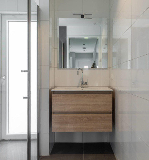Modern lodge bathroom with wooden vanity, wall mirror, faucet, and sleek white tiles on the walls.