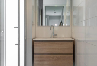 Baño moderno en una cabaña con lavabo de madera, espejo, grifo y azulejos blancos en las paredes.