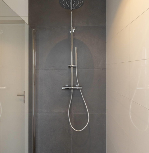Ducha moderna con cabezal tipo lluvia y teleducha, instalada sobre azulejos oscuros en un lodge.