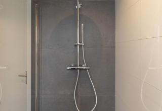 Modern shower with rain showerhead and hand shower, mounted on dark tiles in a lodge bathroom.
