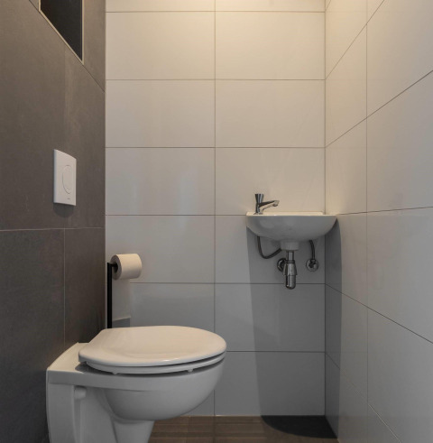 Modern bathroom at a lodge with wall-mounted toilet, small sink, and minimalist gray and white tiles.