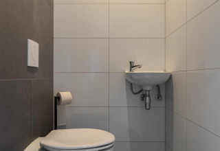 Bagno moderno in un lodge con WC sospeso, piccolo lavandino e piastrelle grigie e bianche minimaliste.