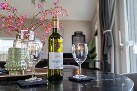 A table with a bottle of wine, two glasses, and flowers at Ecovilla Boszicht Comfort, Latour, Netherlands.