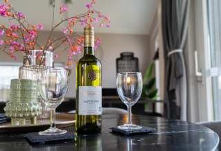 A table with a bottle of wine, two glasses, and flowers at Ecovilla Boszicht Comfort, Latour, Netherlands.