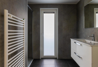 Baño moderno con radiador toallero, lavabo, espejo y puerta de vidrio en Villa Bosrand Comfort.
