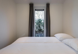 Dormitorio minimalista en Villa Bosrand Comfort en Holiday park Latour, Países Bajos con ventana al jardín.