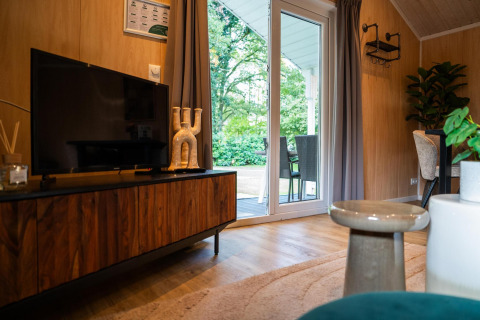 Soggiorno in Lodge Deluxe, Holiday park Latour, Paesi Bassi, con TV, mobile in legno e porta finestra.