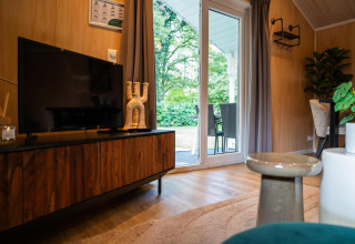 Living room at Lodge Deluxe, Holiday park Latour, Netherlands, with TV, wooden cabinet and patio door.
