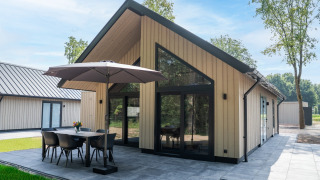 Ecovilla Boszicht Luxe, una cabaña moderna con terraza, mesa exterior y sombrilla en entorno natural.