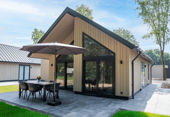 Modern Ecovilla Boszicht Luxe lodge, featuring outdoor dining set and umbrella on a spacious tiled patio.