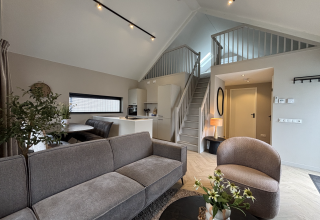 Modern lodge living room with gray sofa and open staircase at Ecovilla Boszicht Luxe, Holiday Park Latour, Netherlands.