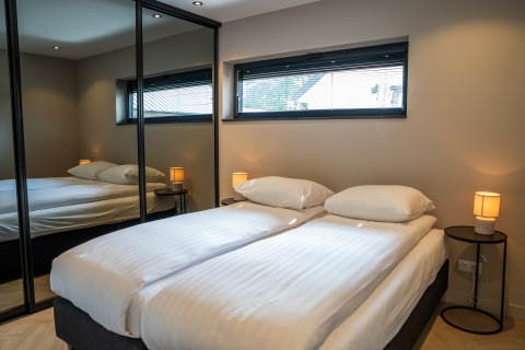 Modern lodge bedroom featuring a double bed, mirrored wardrobe, bedside tables, and a large window.