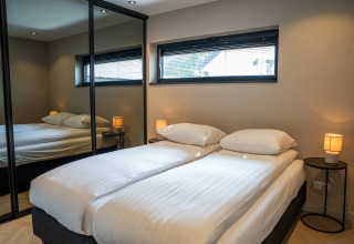 Modern lodge bedroom featuring a double bed, mirrored wardrobe, bedside tables, and a large window.