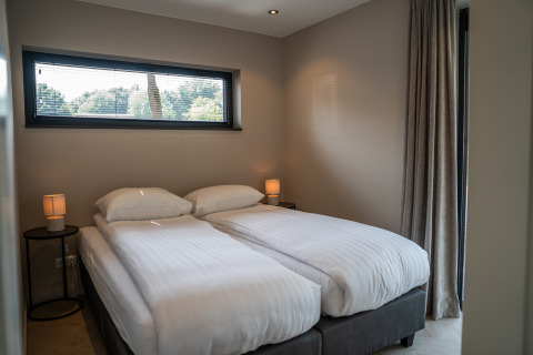 Modern lodge bedroom featuring two single beds with white linens, bedside tables, and a bright window.
