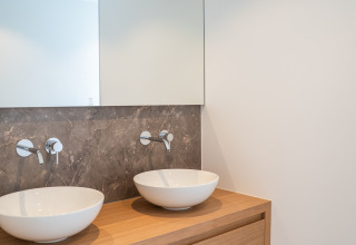 Modern bathroom vanity with twin round vessel sinks on a wood counter, large mirror and marble wall.