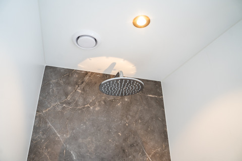 Modern showerhead in a lodge bathroom, featuring a marble wall, ceiling light, and ventilation fan.