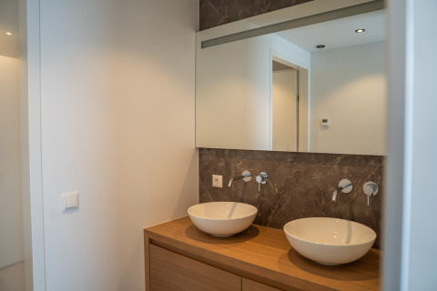 Baño moderno en un lodge, con dos lavabos tipo cuenco, encimera de madera, espejo y pared de mármol.