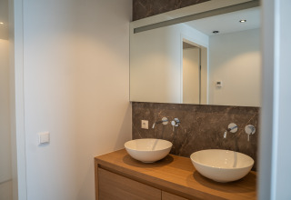 Baño moderno en un lodge, con dos lavabos tipo cuenco, encimera de madera, espejo y pared de mármol.