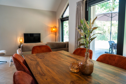 Dining area at Ecovilla Waterzicht Luxe with a wooden table, orange chairs, and terrace view in the Netherlands.