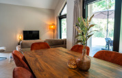 Comedor en Ecovilla Waterzicht Luxe con mesa de madera, sillas naranjas y vista a la terraza en los Países Bajos.