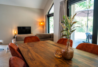 Comedor en Ecovilla Waterzicht Luxe con mesa de madera, sillas naranjas y vista a la terraza en los Países Bajos.
