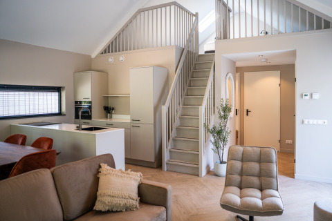 Modern open-plan living space with kitchen, sofa, and stairs in Ecovilla Waterzicht Luxe, Latour, Netherlands.
