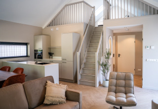 Modern open-plan living space with kitchen, sofa, and stairs in Ecovilla Waterzicht Luxe, Latour, Netherlands.