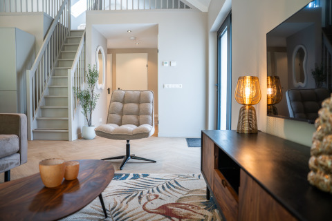 Contemporary living room at Ecovilla Waterzicht Luxe with cozy chair, staircase, and ambient lighting in NL.