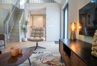 Contemporary living room at Ecovilla Waterzicht Luxe with cozy chair, staircase, and ambient lighting in NL.