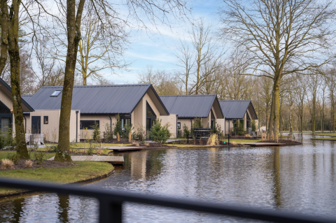 Ecovilla Waterzicht Luxe lodge with modern rooftops beside a pond, surrounded by trees in a calm setting.