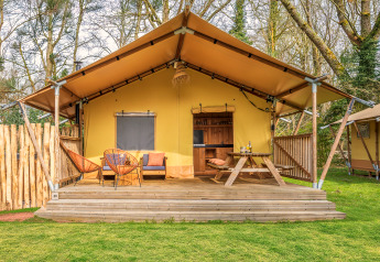Safari-telt med træterrasse, siddepladser og piknikbord i et skovområde, perfekt til glamping.