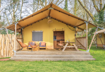 Tente safari avec terrasse en bois, espace détente et table de pique-nique en forêt, parfaite pour le glamping.