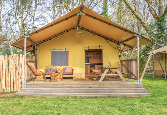 Safari-telt med træterrasse, siddepladser og piknikbord i et skovområde, perfekt til glamping.
